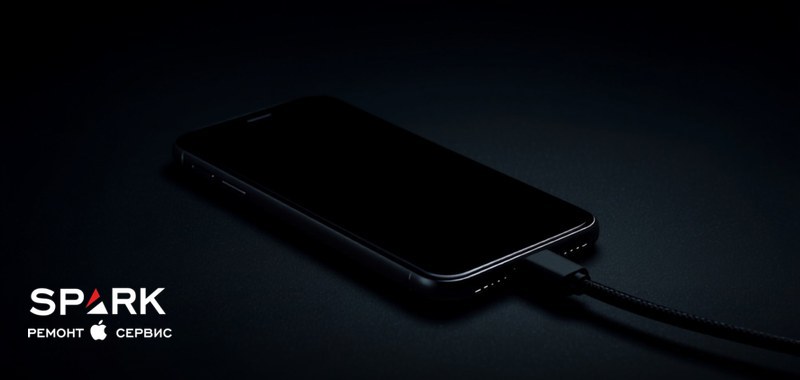 iPhone лежит на тёмном столе, в нижний разъём подключён плетёный кабель зарядки